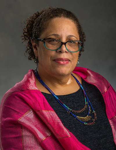 Woman of color with glasses in a black top and pink jacket