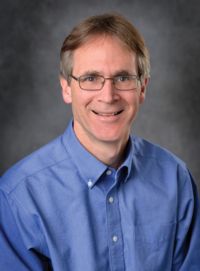 Portrait photo of Eric Hegg, fair complection, brown hair with glasses in blue shirt