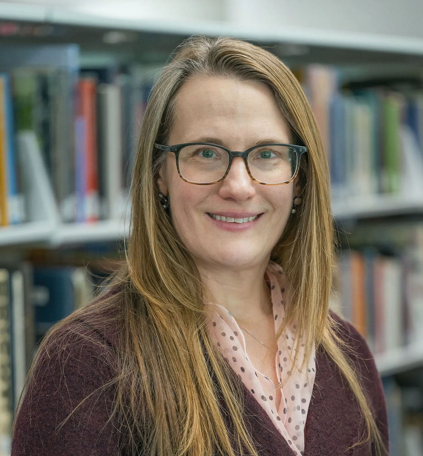 Andrea Case posing for a portrait photo in front of a bookcase.