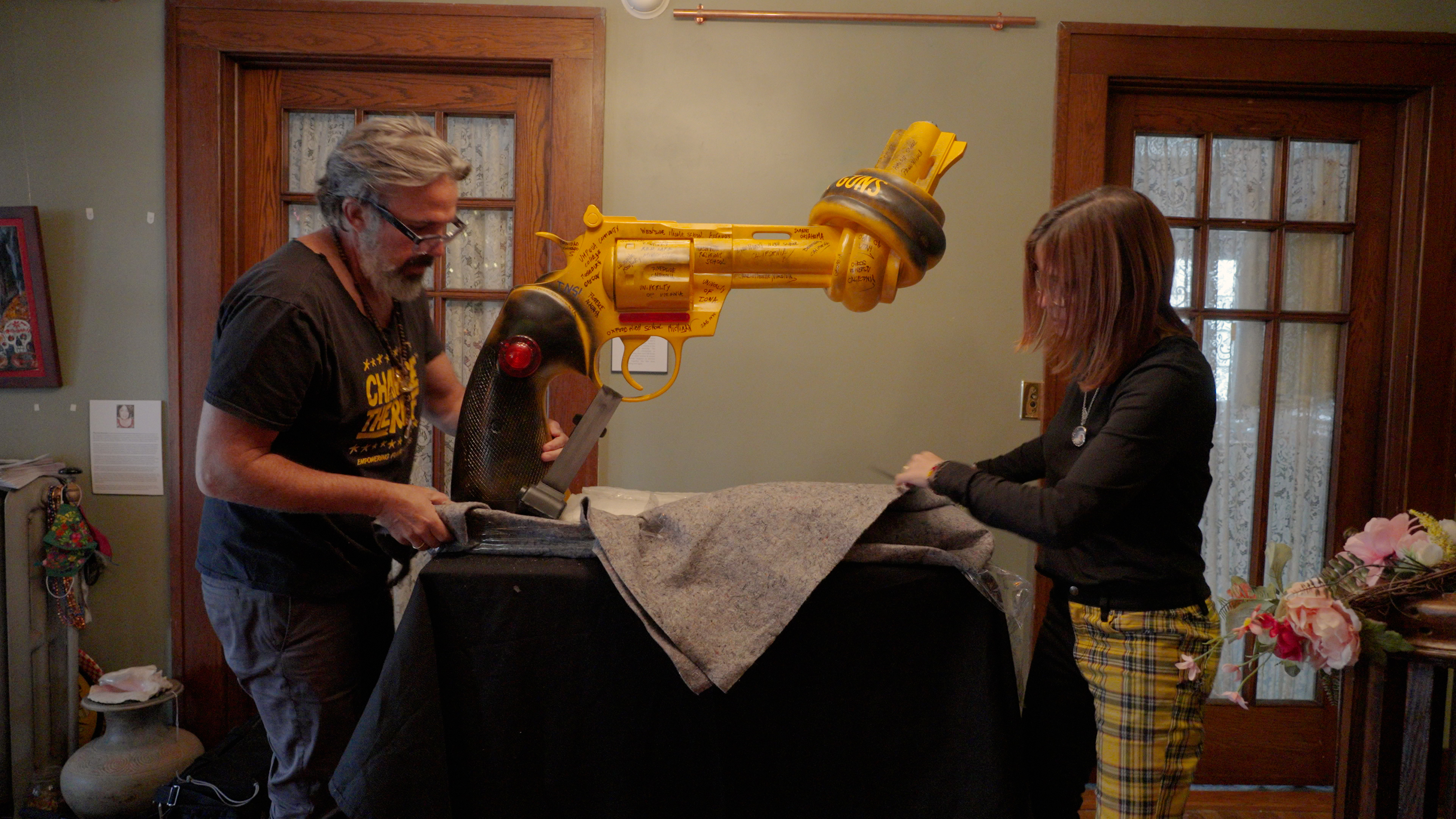 A man and woman moving a sculpture of a yellow gun with a knot in it