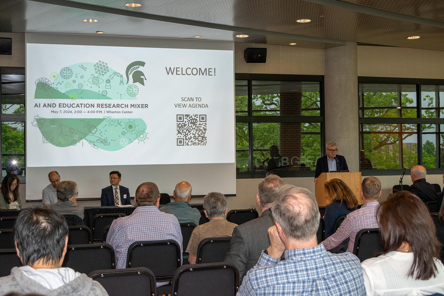 A group of people in front of a presentation screen, listening to a lecture