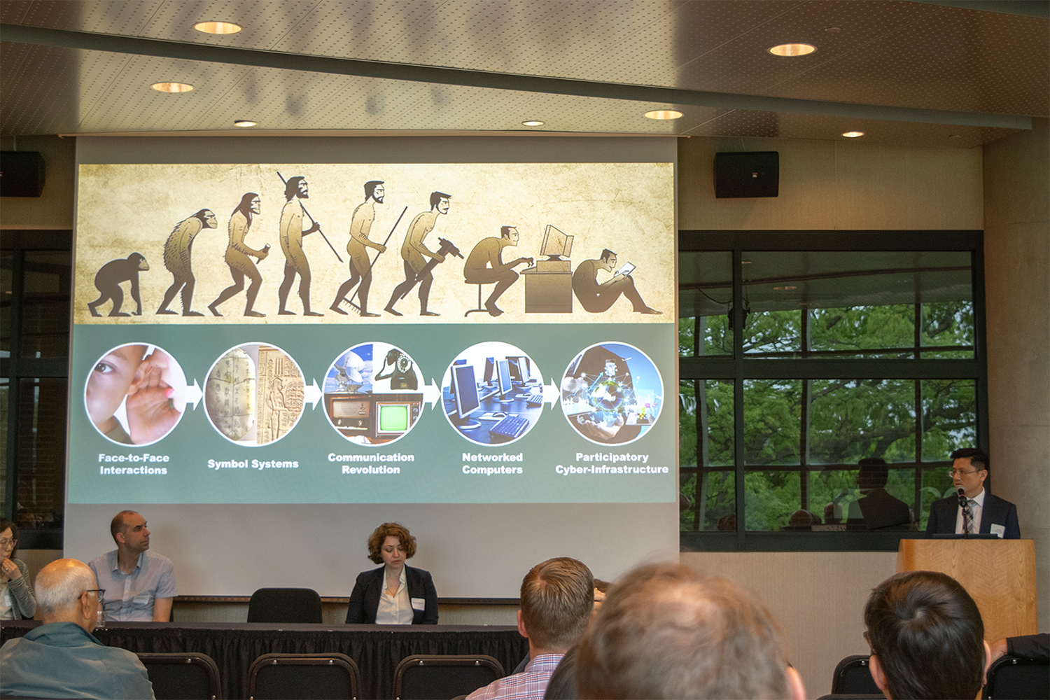 A group of people in front of a presentation screen, listening to a lecture