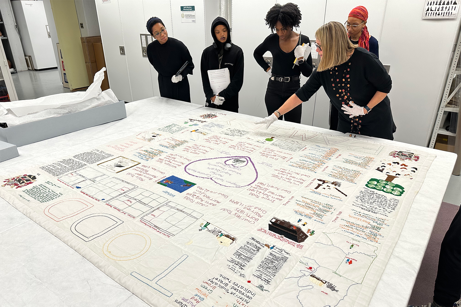 Five people looking at a large historical quilt. 