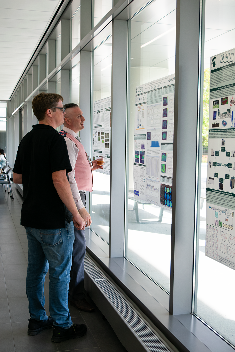 Two men looking at research posters on a window.