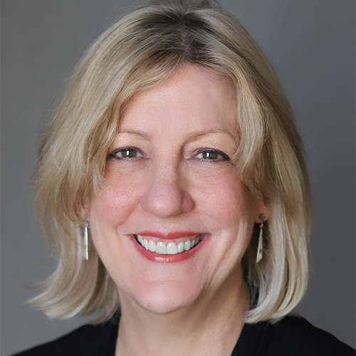 A woman with short blonde hair, and earrings, wearing a dark top, smiling