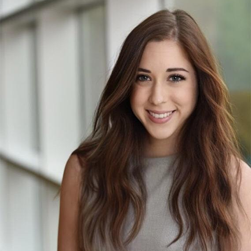 A woman with long brown hair, and sleeveless grey top, smiling