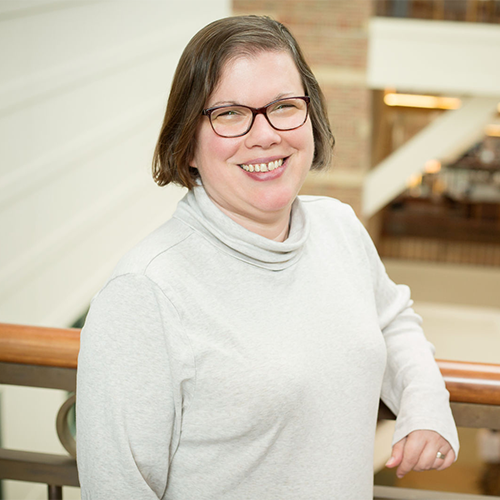 A woman with short dark hair and glasses, wearing a white turtleneck sweater