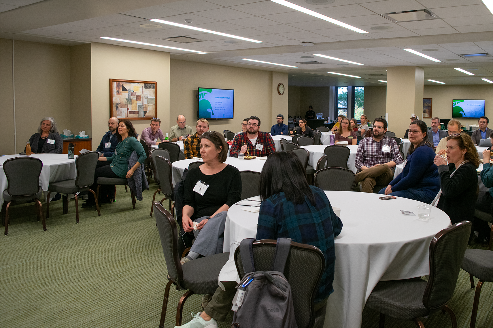 A group of people, sitting at tables and listening to a presentation.