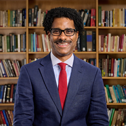 Brian Johnson in a Suit Posing for Headshot Behind Library