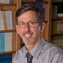 Miles McNall Posing for Headshot in Front of Bookshelves