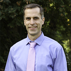 Ryan Sweeder Wearing a Suit Posing for a Headshot in Nature