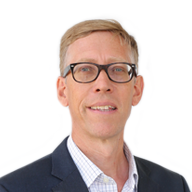 A man with short blonde hair, wearing a suit and dark framed glasses