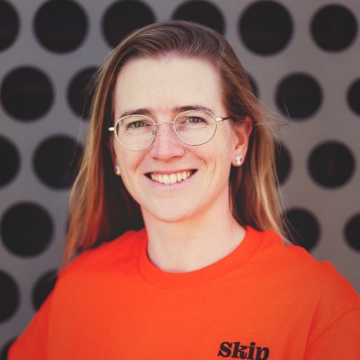 A woman with long hair, wearing thin framed glasses and an orange shirt