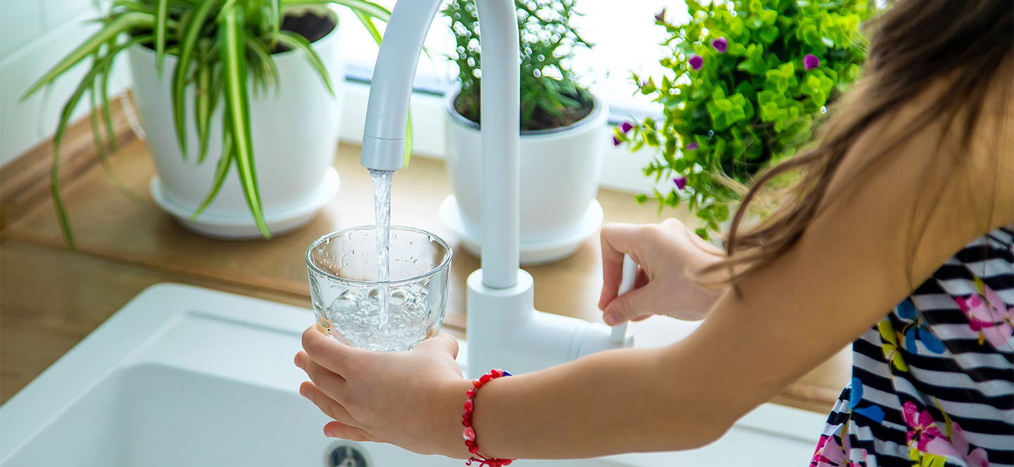 A person filling a glass with water under a faucet