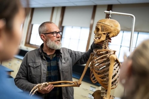 Joe Hefner instructs students using a human skeleton model in class