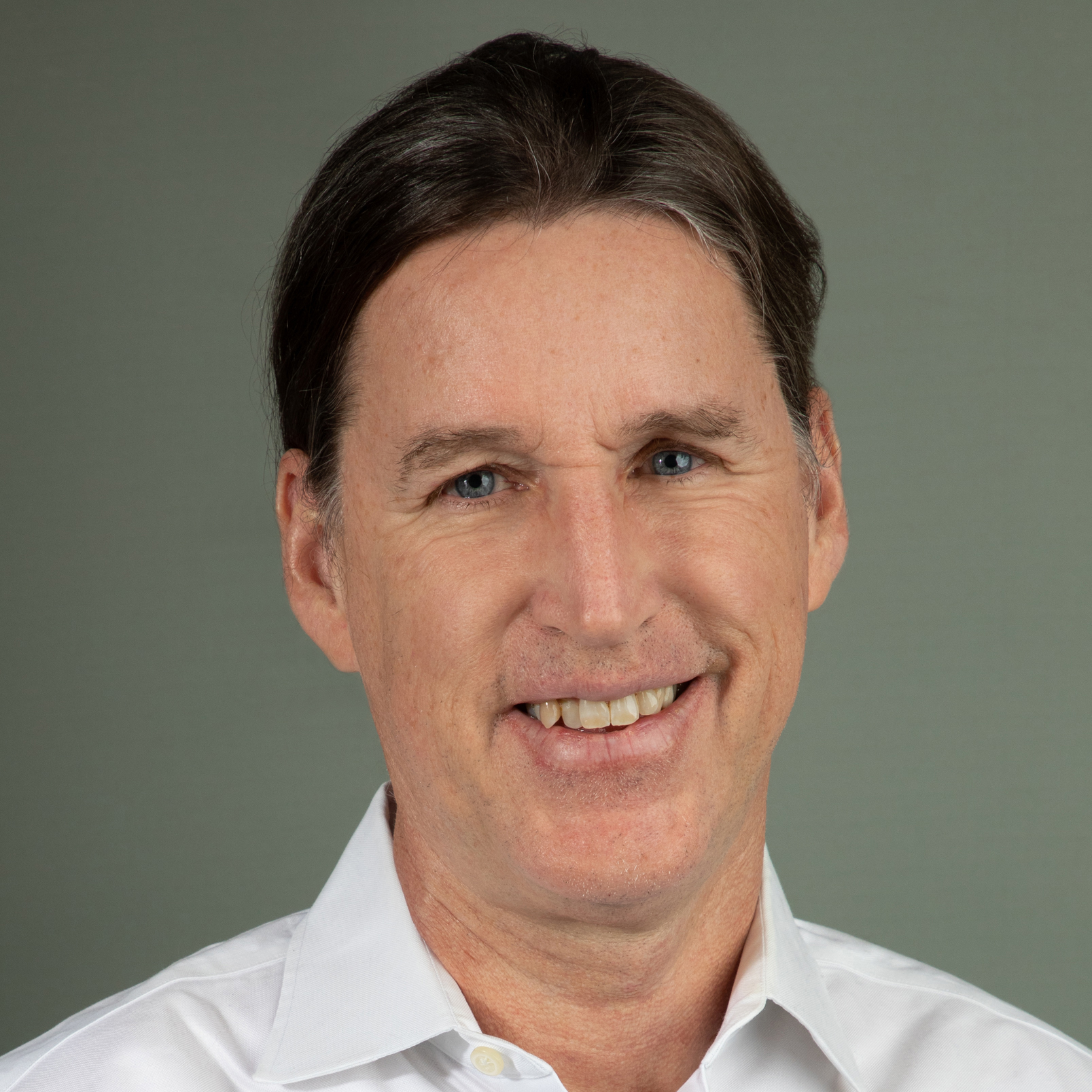 A man with short dark hair, light shirt, in front of a grey background.