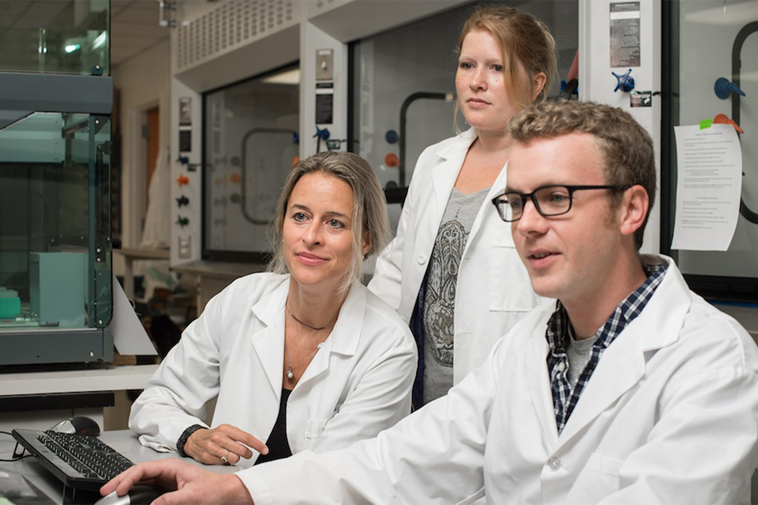 Three people in white coats gathered around a computer