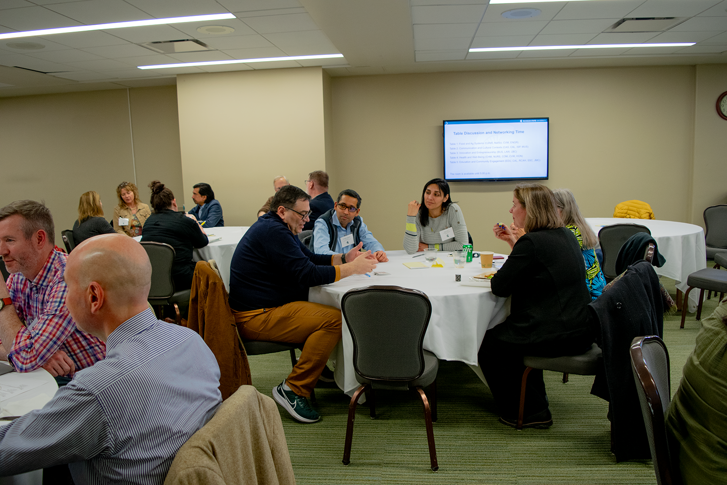 A group of people in a room, sitting at tables and having conversations.