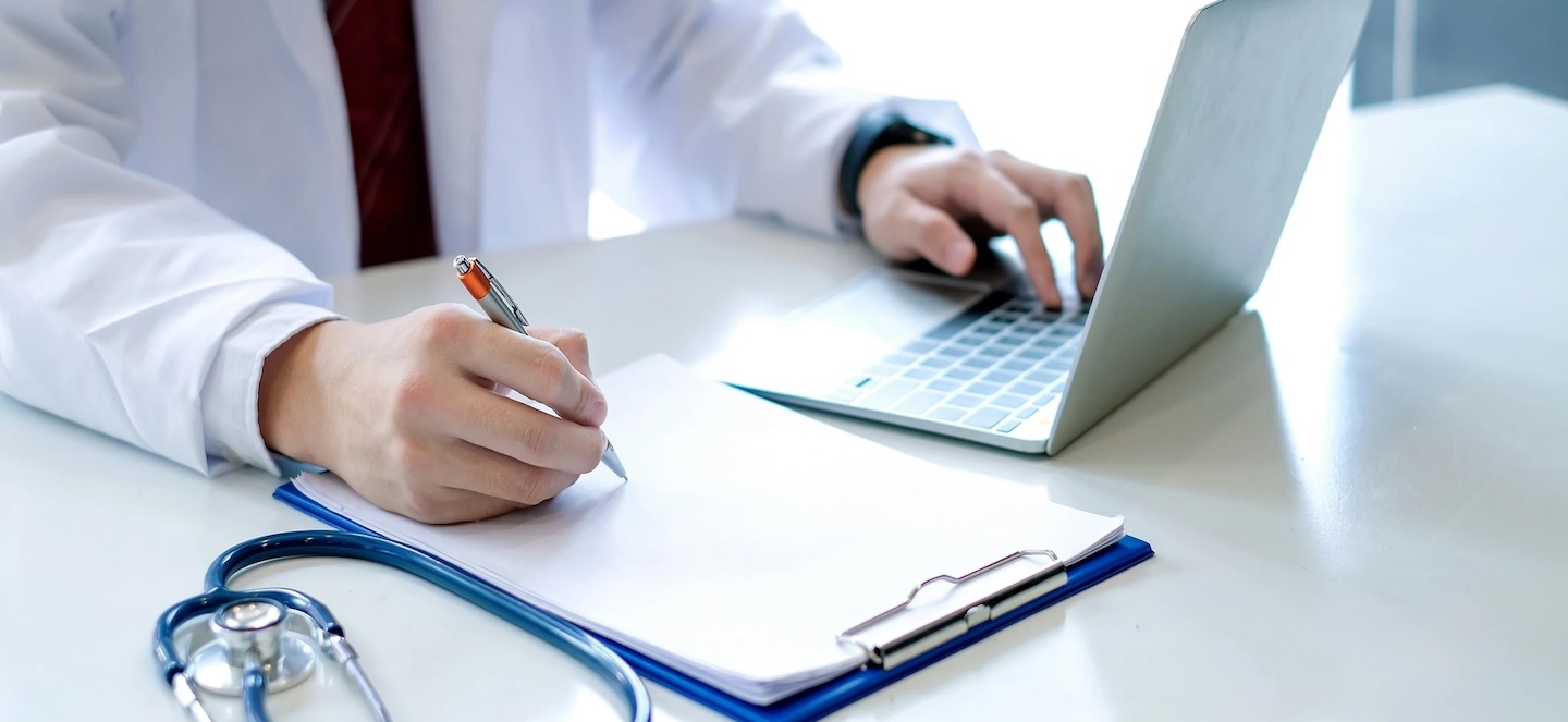 Doctor taking notes and browsing computer
