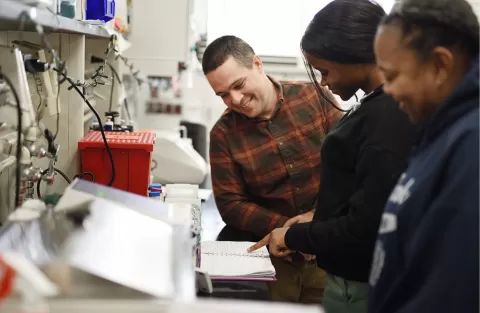 Two students with a mentor working at a lab bench