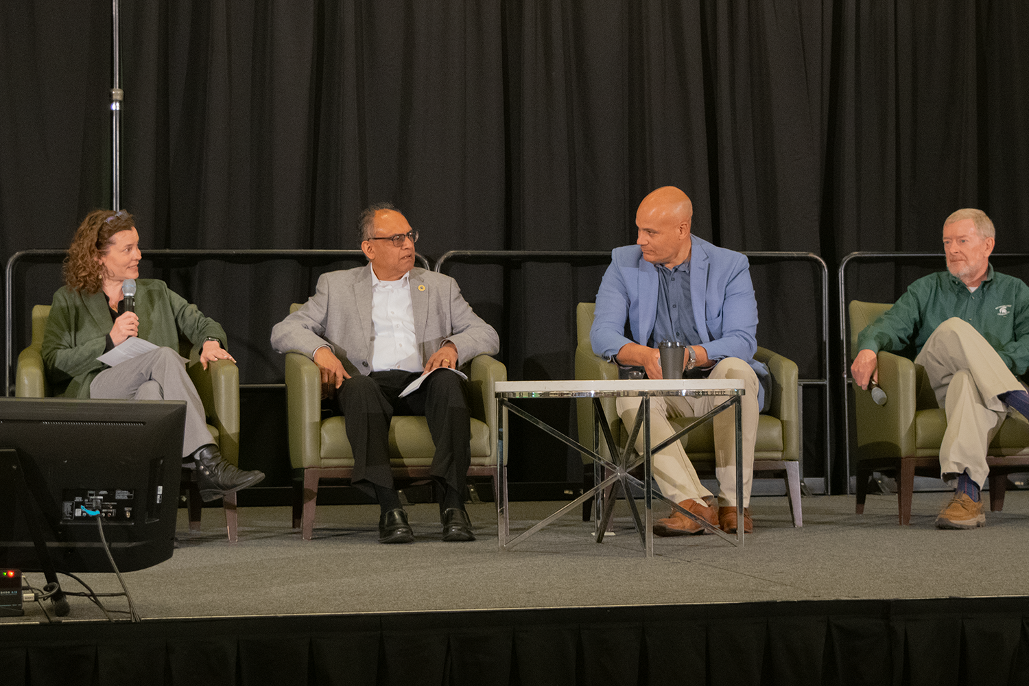 Four people sitting on a stage in chairs, having a conversation.