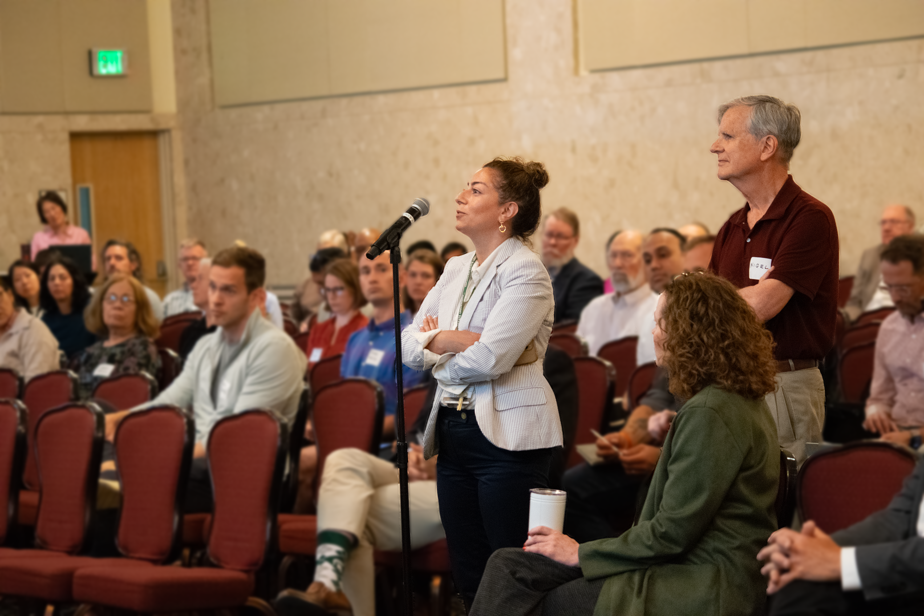 A person stands at a microphone, participating in a Q&A session amongst several people in chairs. 