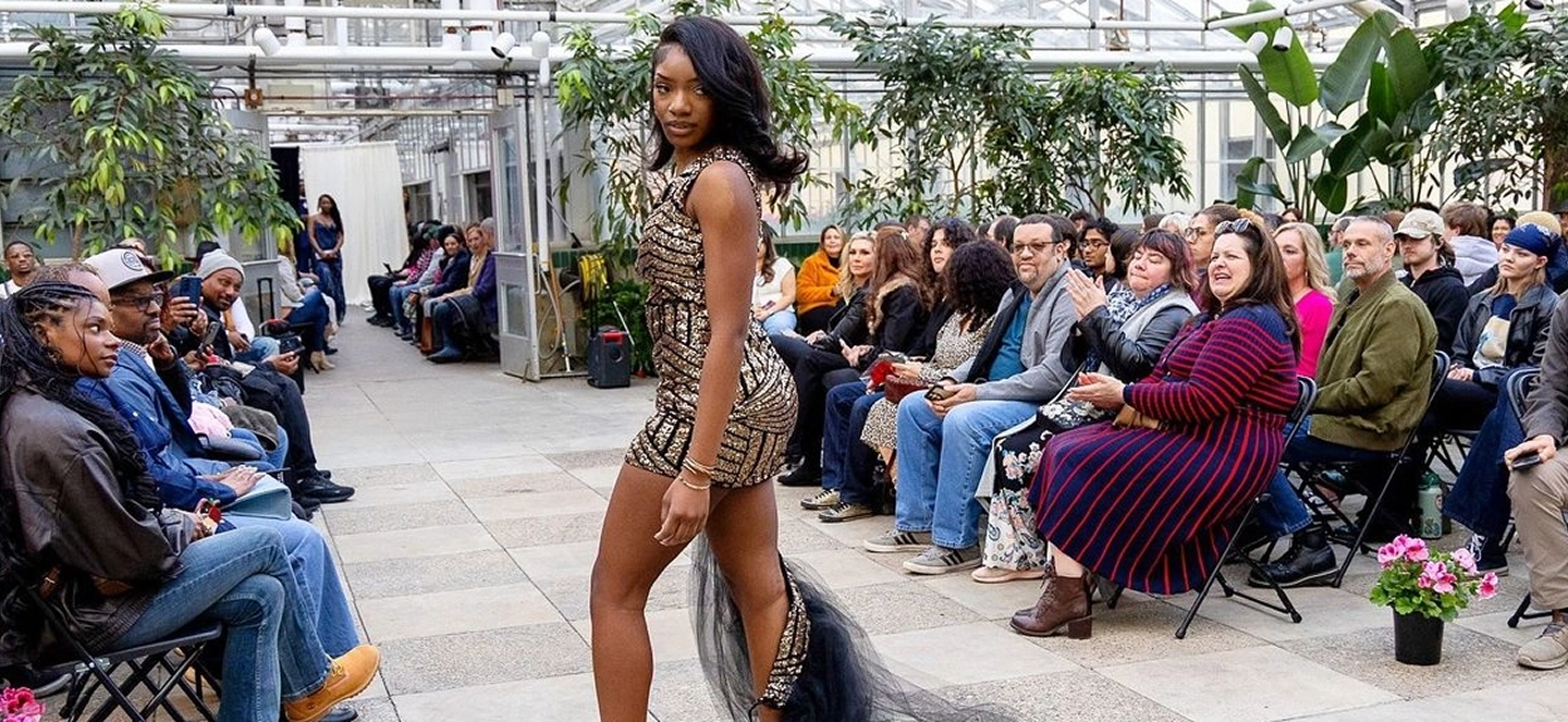 Model in greenhouse wearing a gold and black dress