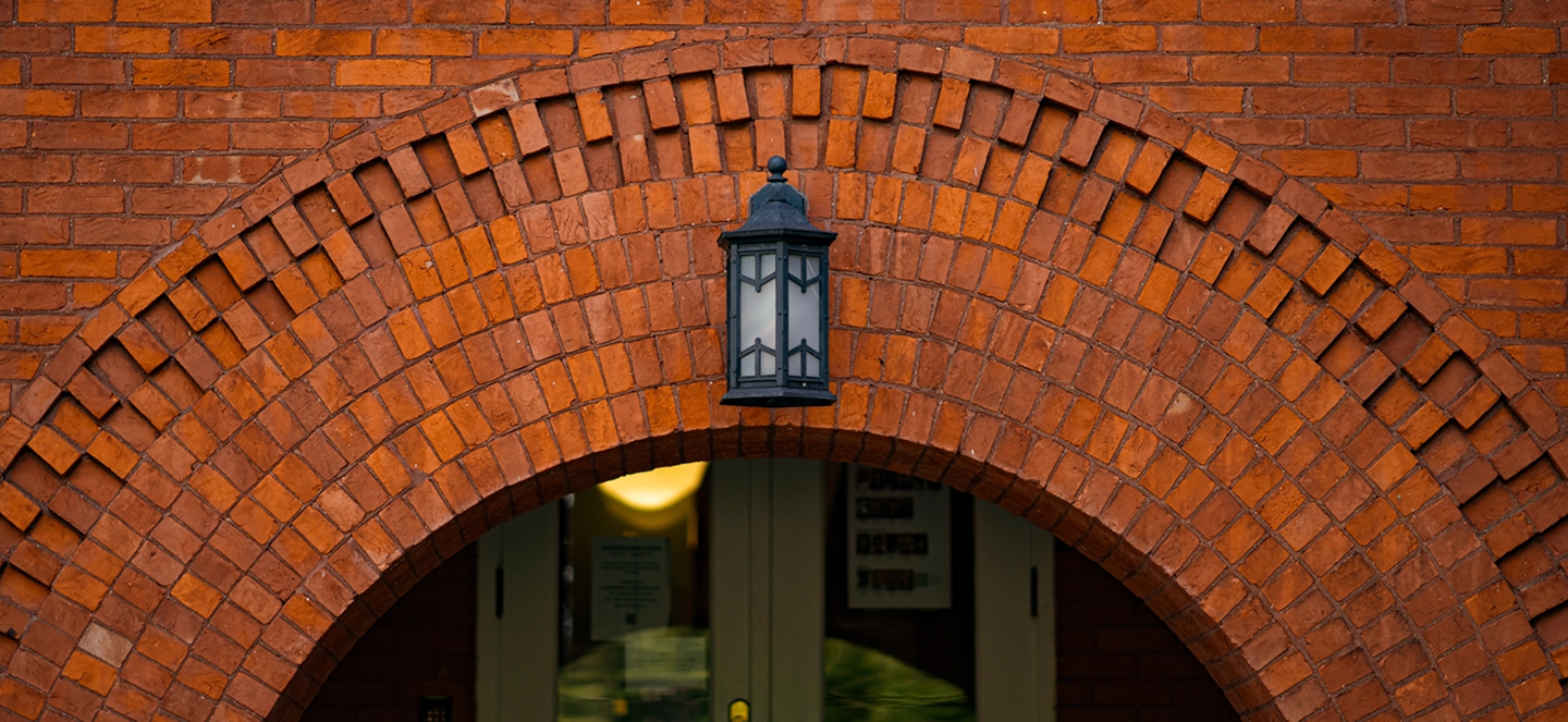 A brick building featuring an arched entrance and a lantern mounted above the doorway