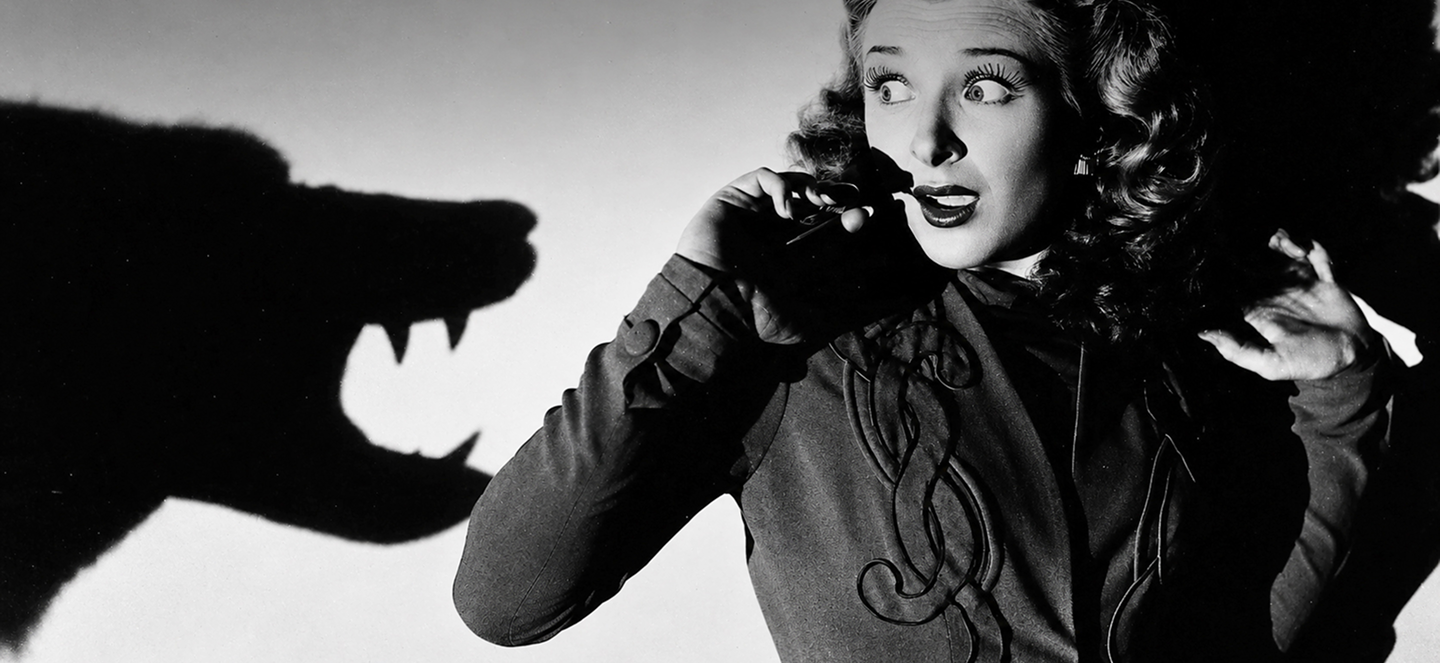 Black-and-white image of a frightened woman pressed against a wall as a large, monster-like shadow looms next to her 