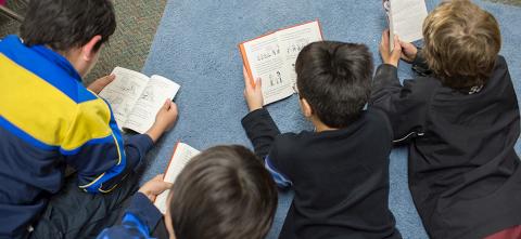 Children laying on a carpet reading books. 