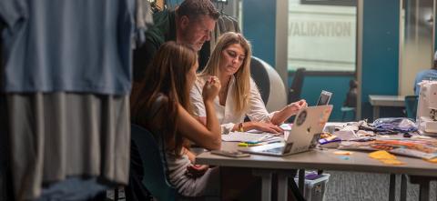 Two students working with an advisor while looking at a laptop.