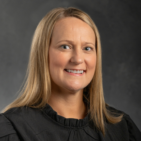 A woman with shoulder length blonde hair, wearing a dark blouse