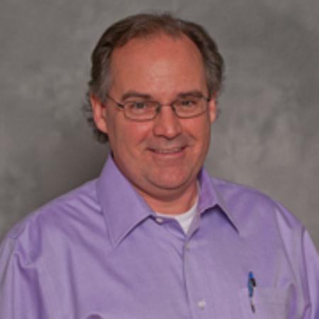 A man with dark hair, glasses, wearing a purple collared shirt