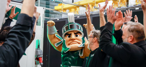 MSU's mascot, Sparty, raising hands with a crowd