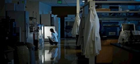 A person hunching over a lab fridge