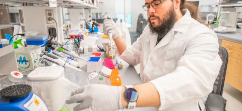 Researcher in a lab coat using a micropipette in a biomedical laboratory