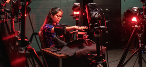 A person sits in a lab with lights and cameras extending her arm into a motion-tracking device