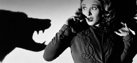 Black-and-white image of a frightened woman pressed against a wall as a large, monster-like shadow looms next to her 
