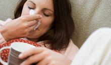 Woman with a cold, blowing her nose with tissue.