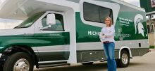 Woman standing in front of RV with spartan logo and colors