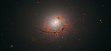 A supermassive black hole surrounded by glowing orange accretion disk material in space.